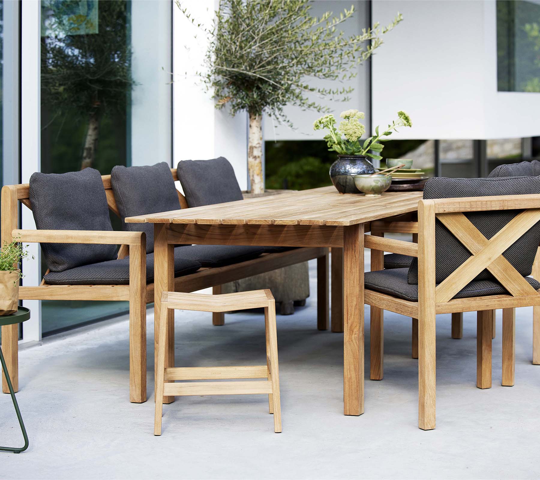 Een houten tafel omringd door stijlvolle stoelen en een bank, met zachte kussens en decoratieve planten voor een uitnodigende zitplek.