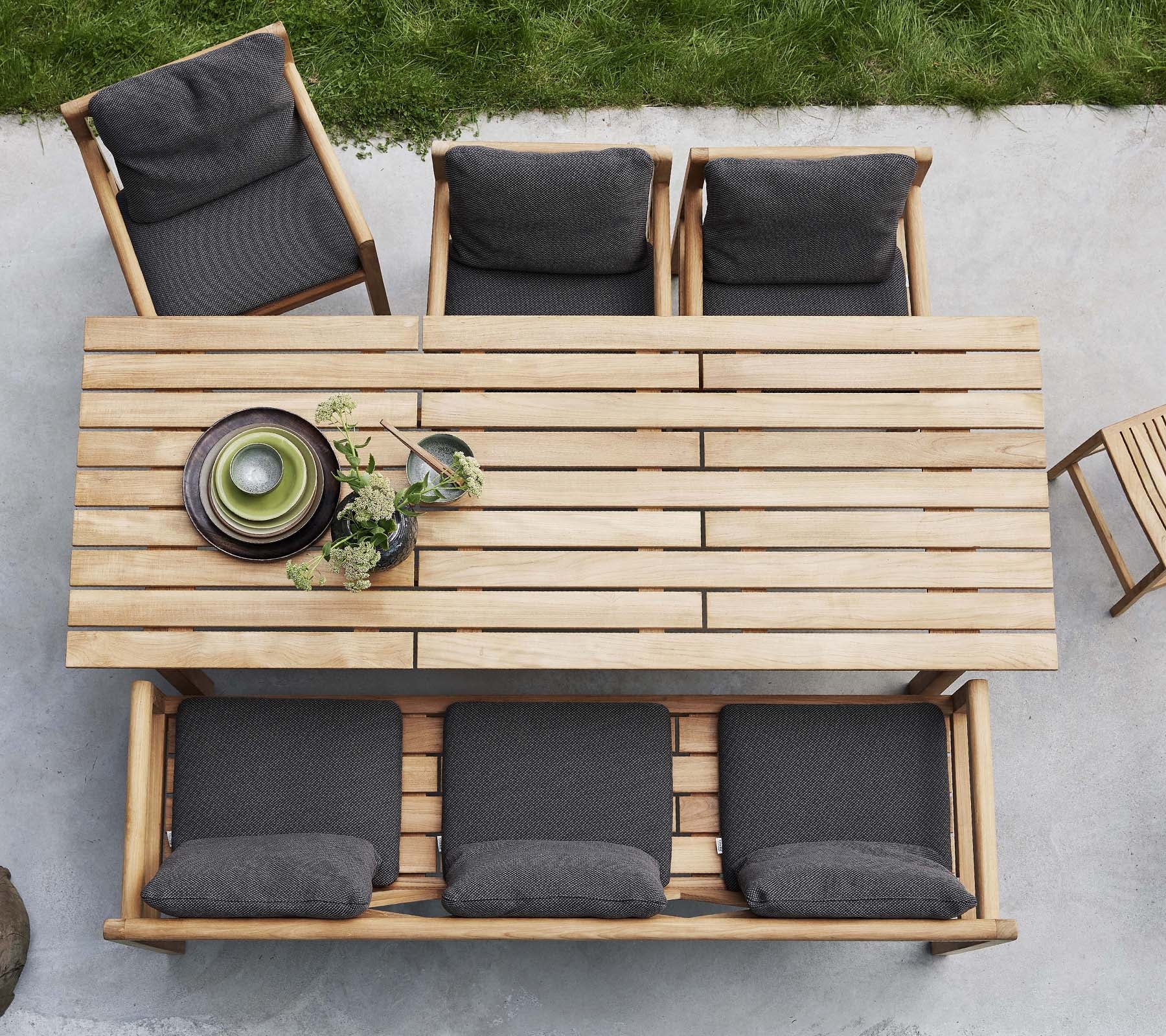 Een houten tafel vergezeld van vier stoelen, elk met donkere kussens, met decoratieve borden en groen op de tafel.