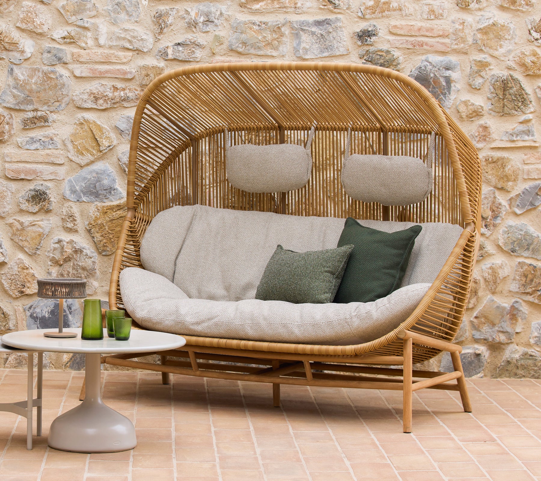 Hive bank met pluche kussens en groene accenten naast Glaze salontafels, tegen een natuurlijke stenen achtergrond.