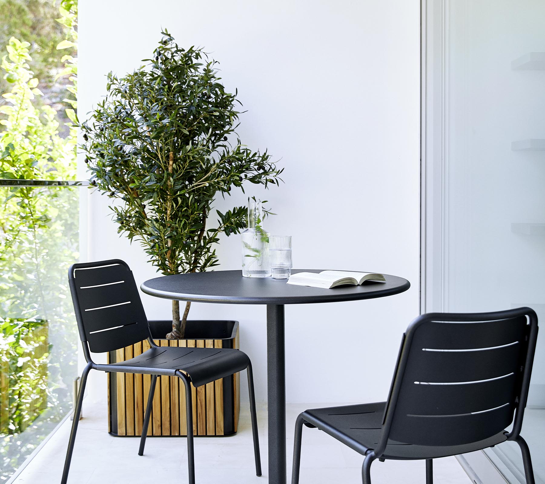 Een moderne eetopstelling met een ronde tafel, twee zwarte stoelen en een potplant, die een stijlvolle en uitnodigende sfeer creëert.