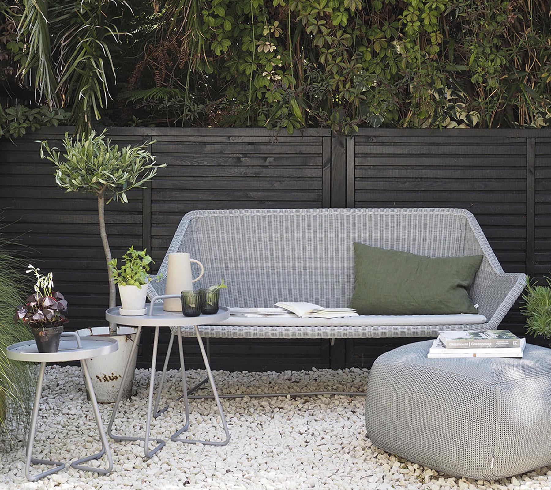 Minimalistische buitenmeubelopstelling met een stijlvolle bank, bijzettafels en decoratieve planten op een kiezeloppervlak.