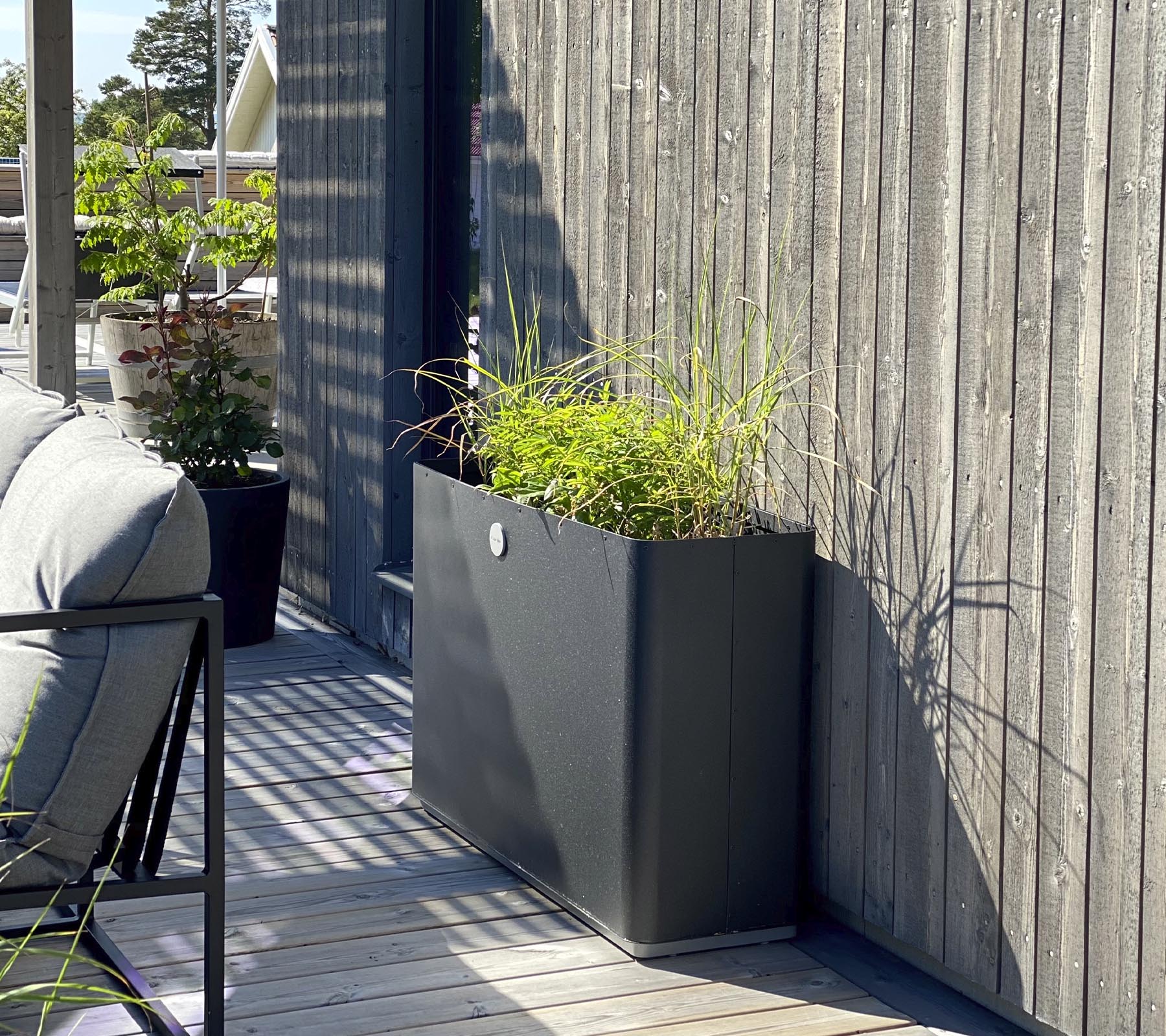 Een strakke, moderne plantenbak met levendige groene planten staat tegen een gestructureerde houten muur en complementair aan de omliggende ruimte.