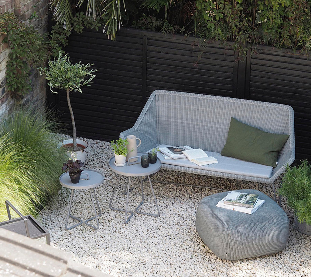 Moderne grijze bank met groene kussen en grijze salontafel in een minimalistisch loungegebied.