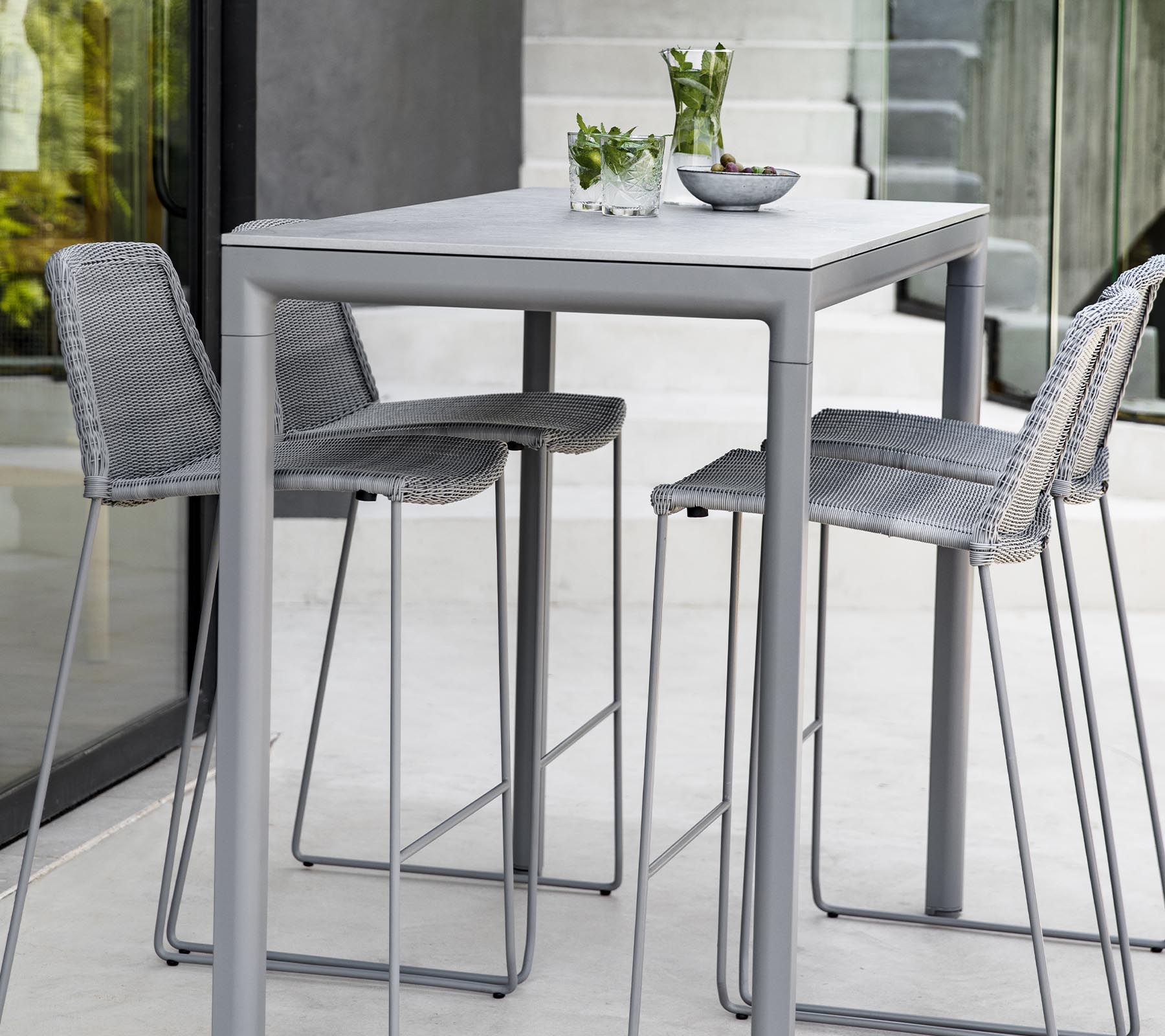 Een moderne grijze tafel met drie bijpassende krukken, met decoratieve planten en een schaal op het tafelblad.