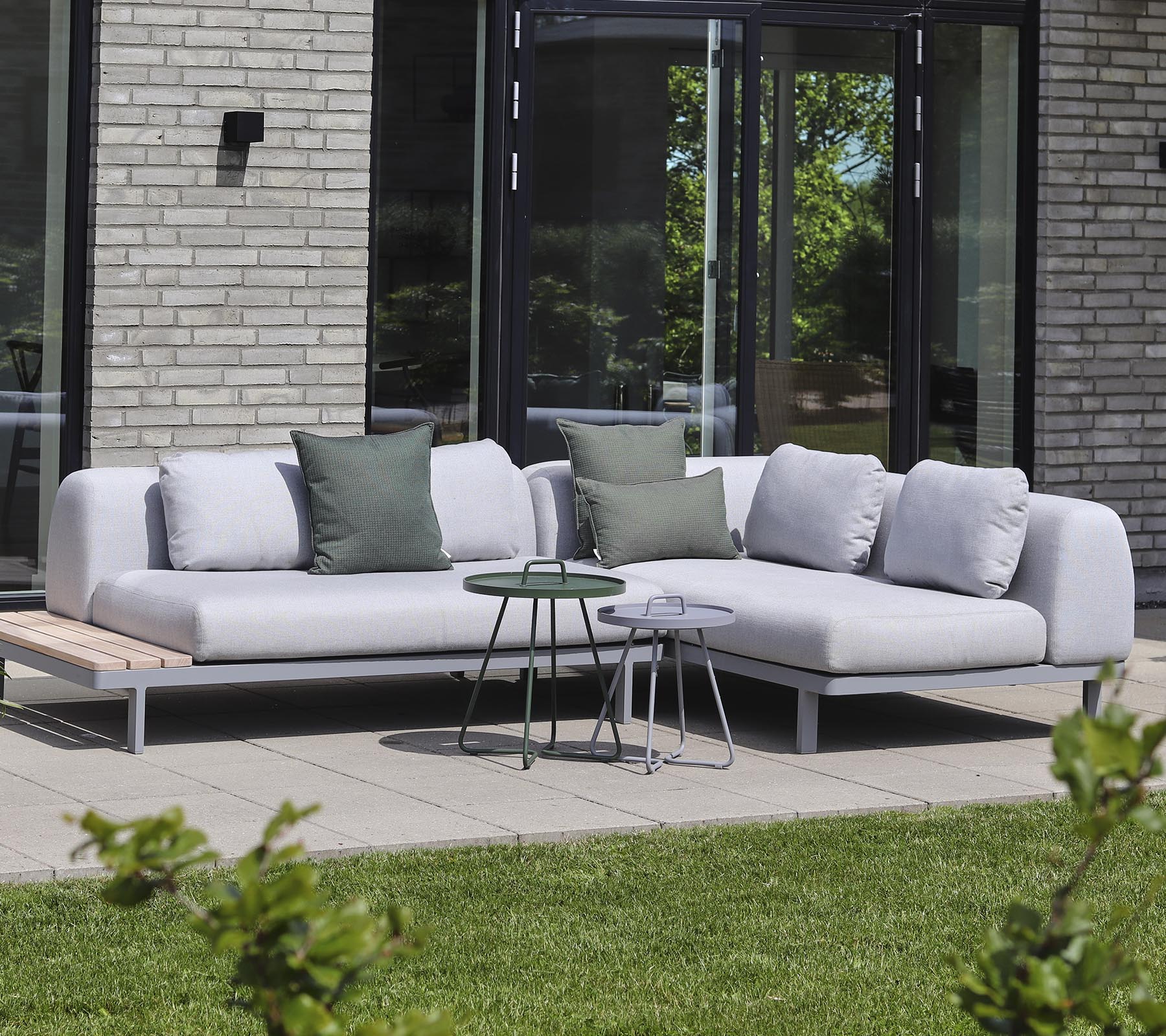 Moderne sectionele bank in lichte stof met decoratieve kussens, gecombineerd met kleine bijzettafels in een rustige setting.