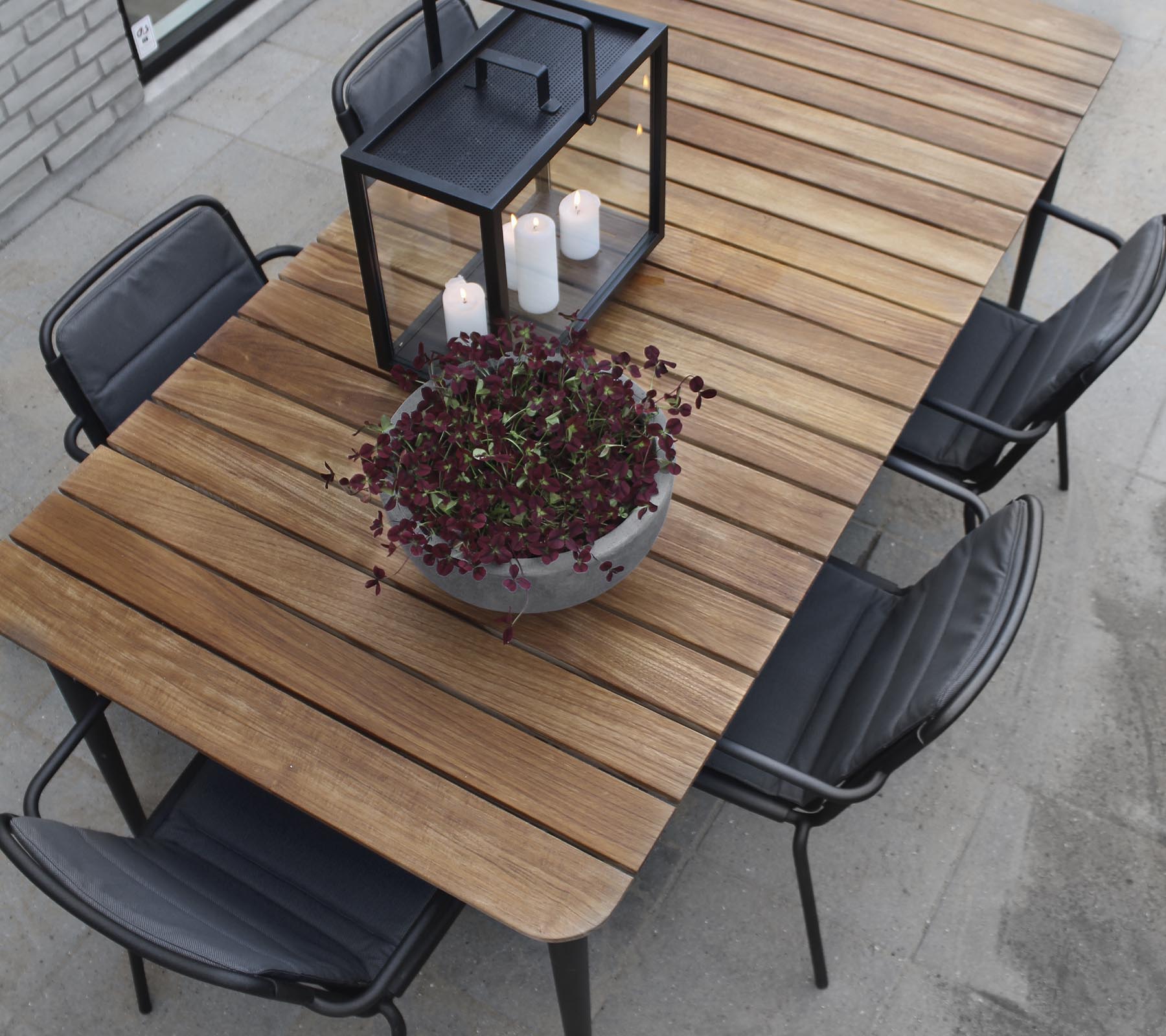 Een houten tafel met zwarte stoelen, met een grote plantenbak en een kaarsenlantaarn in het midden.