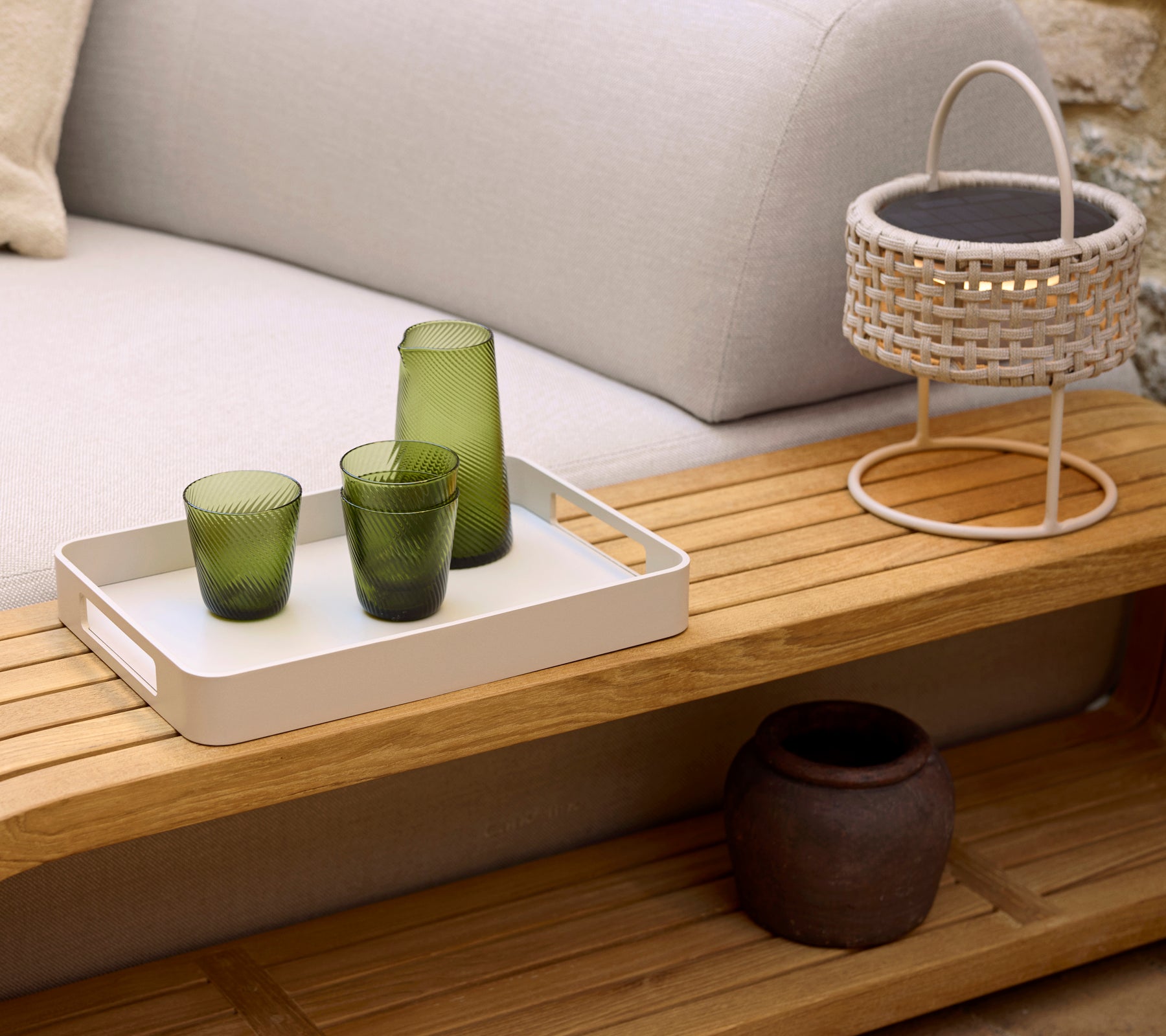 Een gezellig salontafel met een witte dienblad, drie groene glazen, een geweven lamp en een decoratieve pot, die een serene ambiance versterkt.