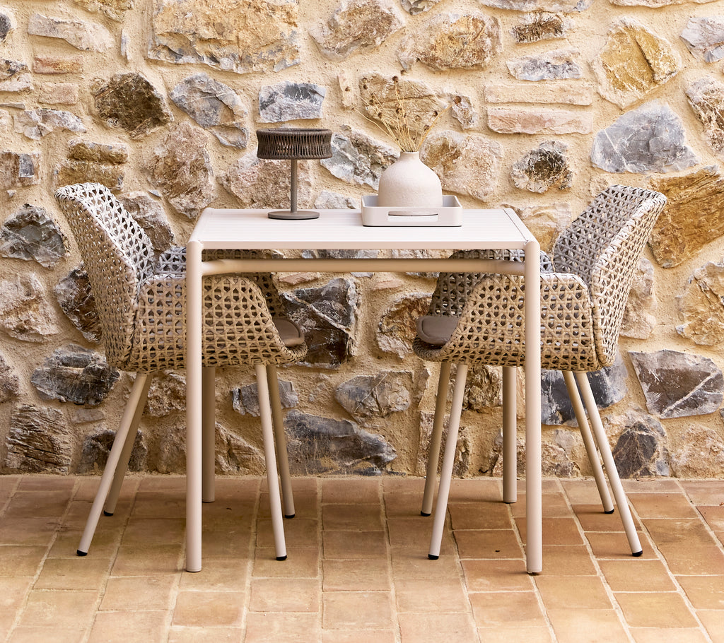 Een kleine donkergrijze illusielamp op een Bliss-tafel met twee Vibe-stoelen, omringd door een gestructureerde stenen muur.