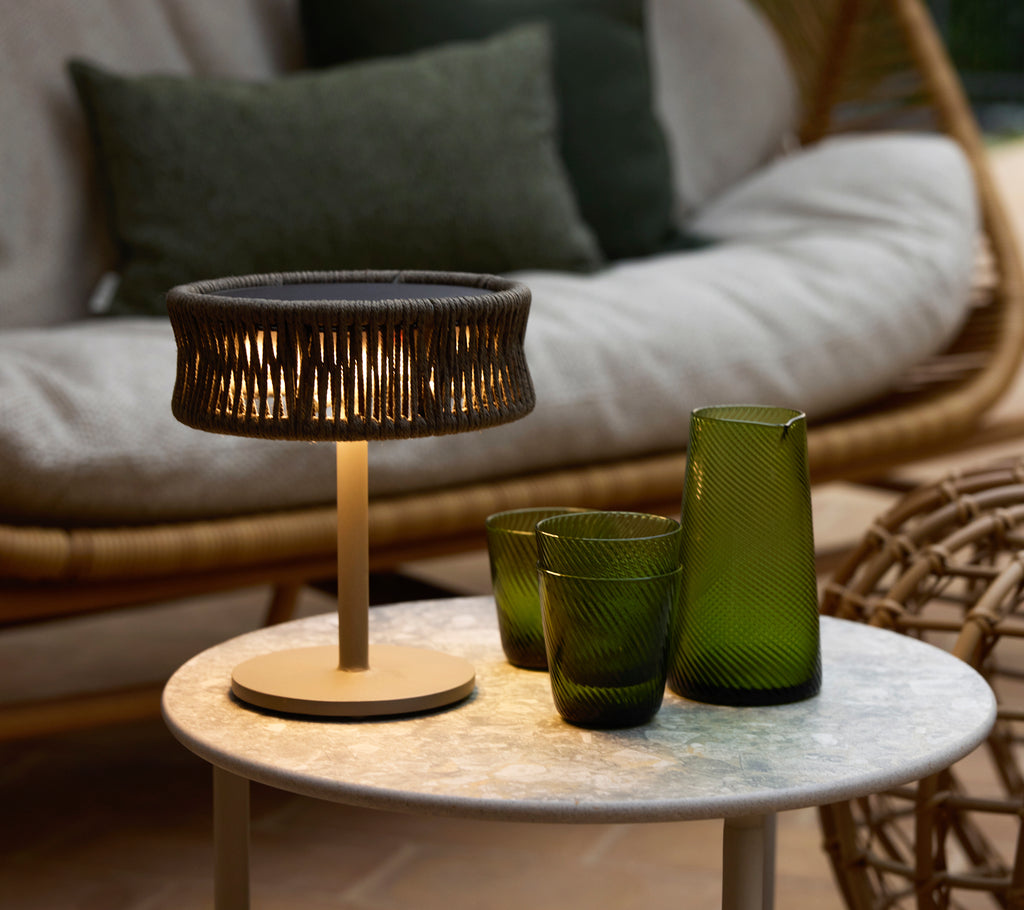 Een kleine donkergrijze illusielamp op een marmeren salontafel, vergezeld van groene decoratieve glasvazen en een gezellige zithoek.