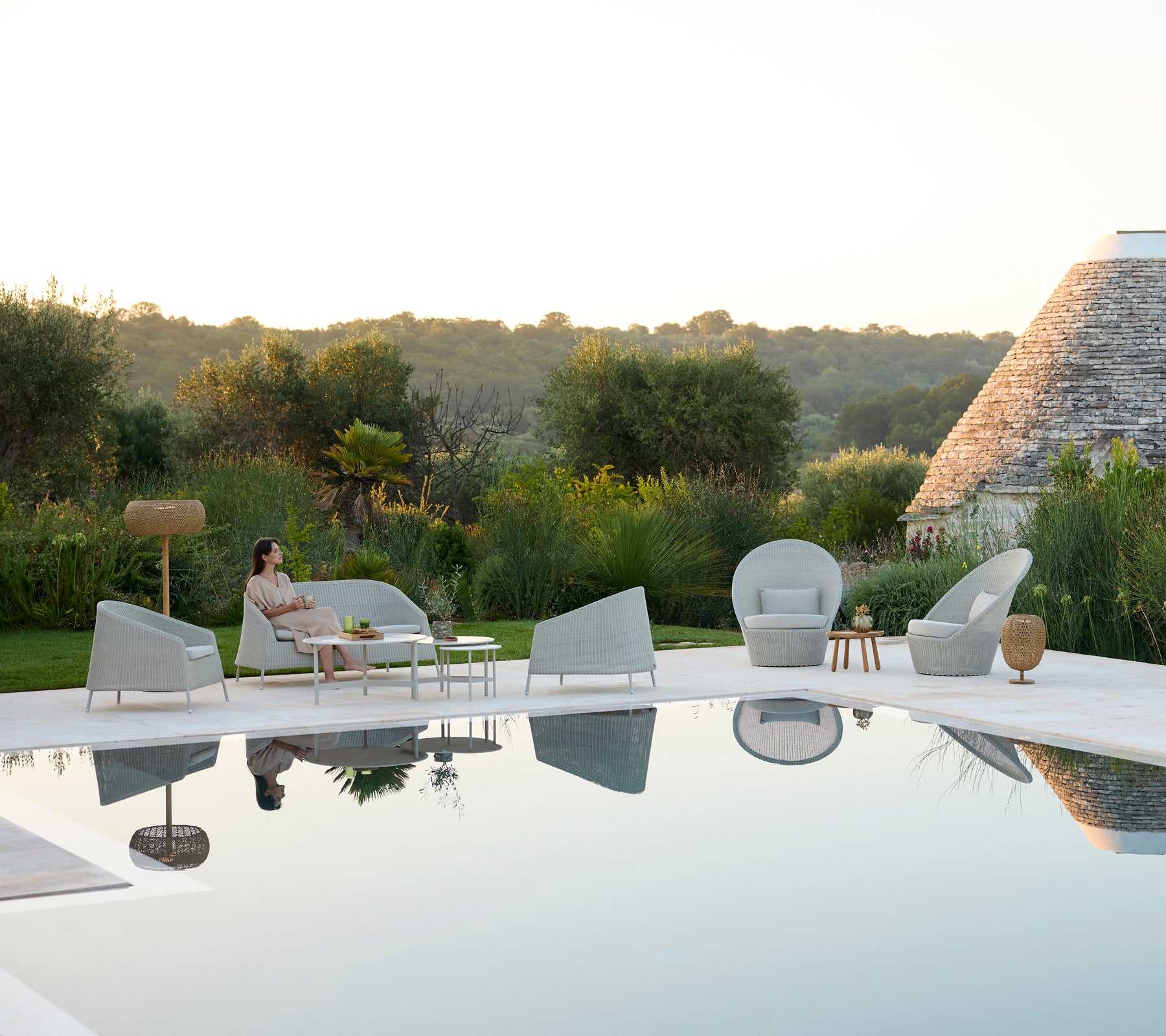 Moderne buitenlounge met grijze stoelen en een witte tafel bij een zwembad.