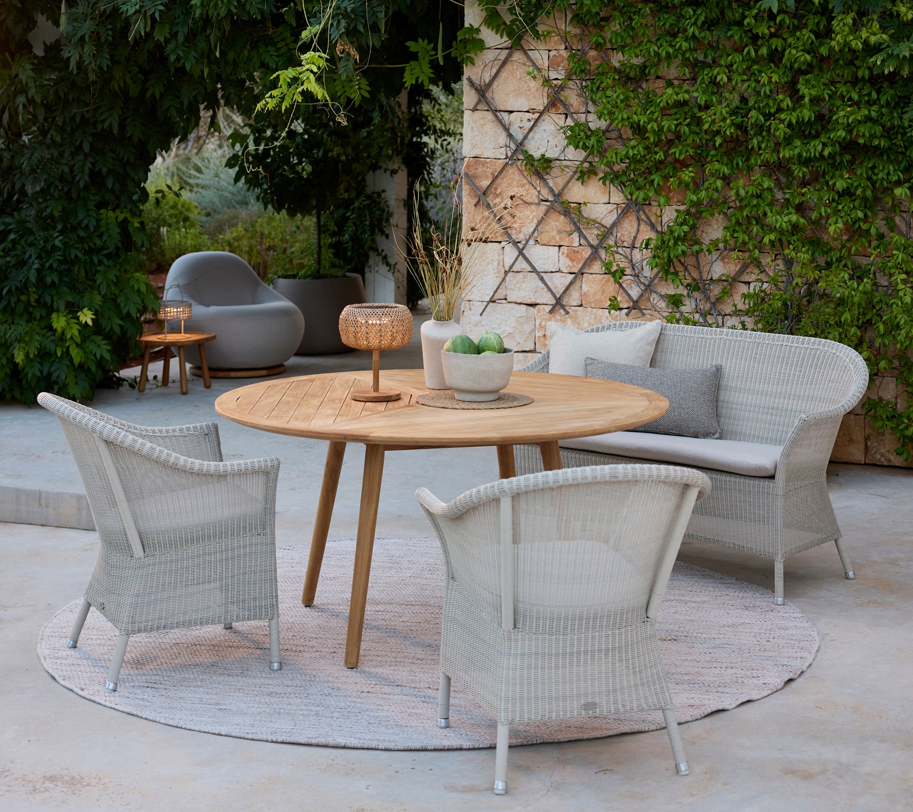 Moderne loungegebied met grijze stoelen, een ronde houten tafel en een grijze bank omringd door groen.