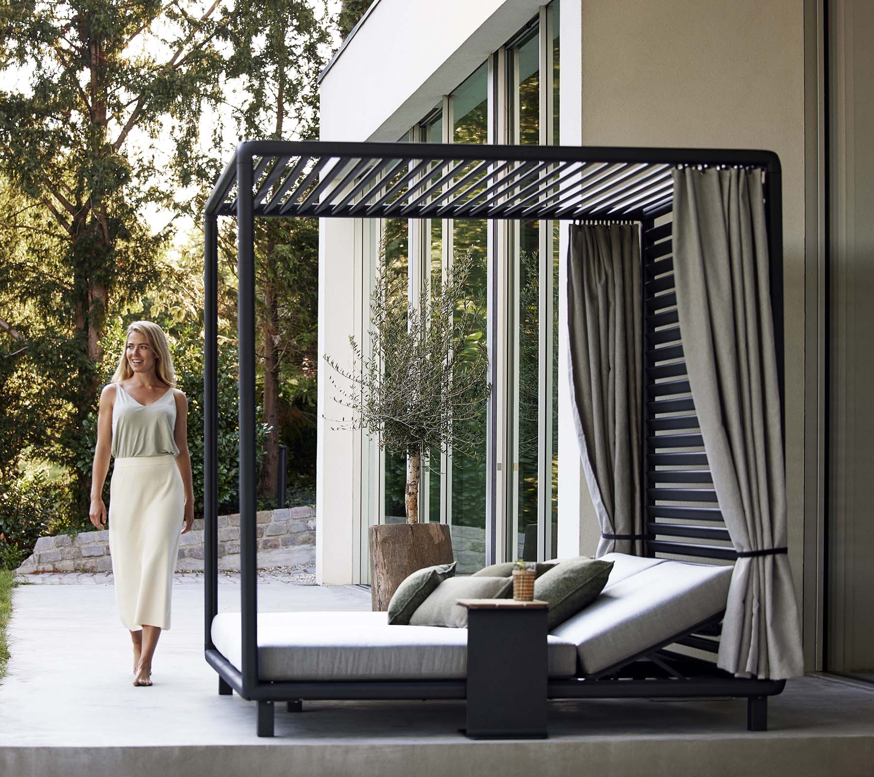 Een stijlvolle cabana met een strak ontwerp, zachte kussens, gordijnen en een klein bijzettafeltje, gelegen in een serene, natuurlijke omgeving.