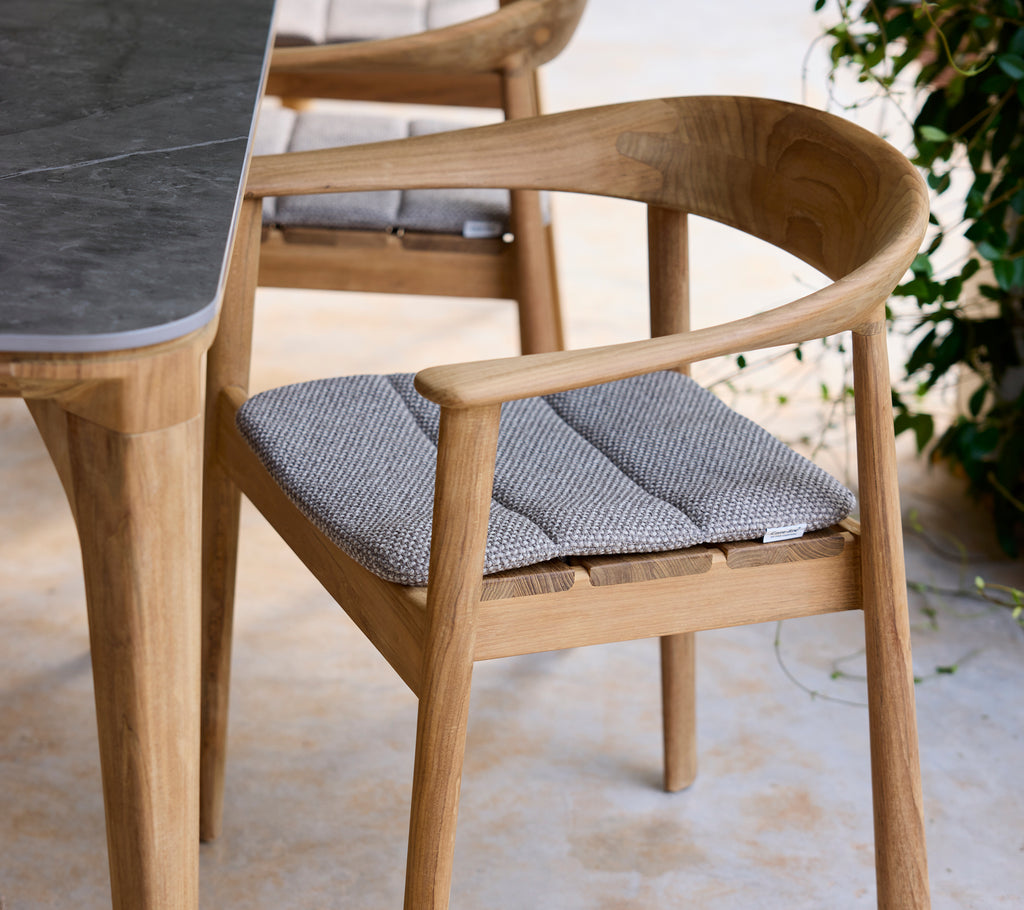 Moderne houten stoel met grijze kussen naast een tafel in een lounge-setting.