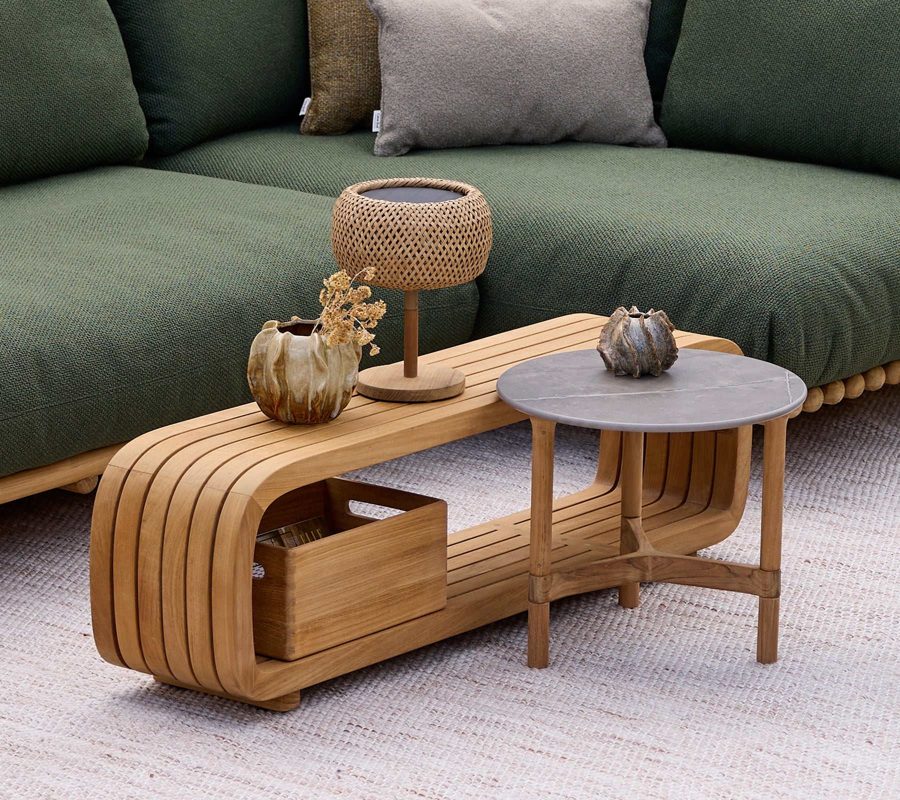 Moderne houten salontafel met een grijze bijzettafel, lamp en decoratieve vaas in een lounge-instelling.