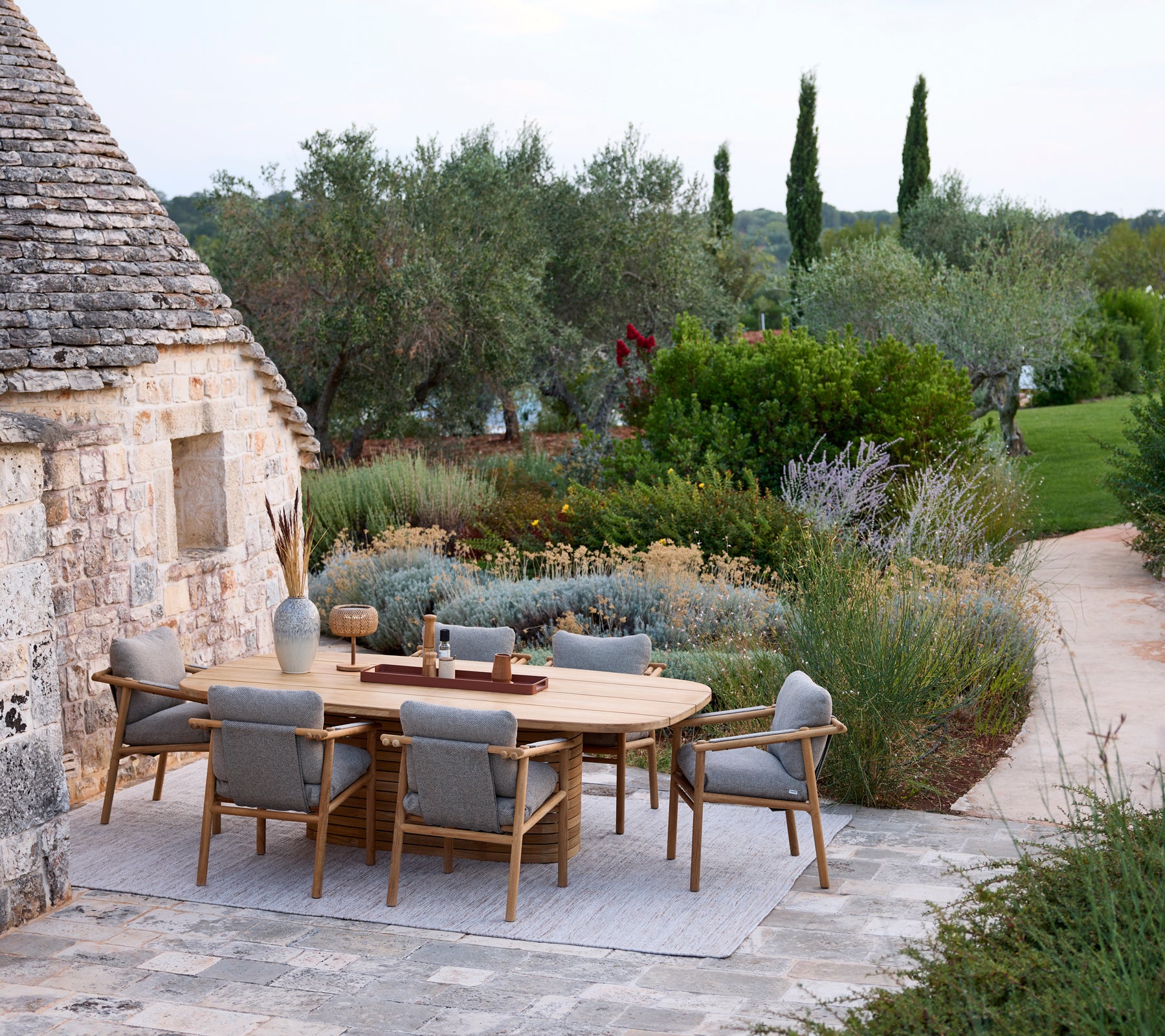 Moderne buitentuinset met een ronde tafel en grijze stoelen omgeven door groen.