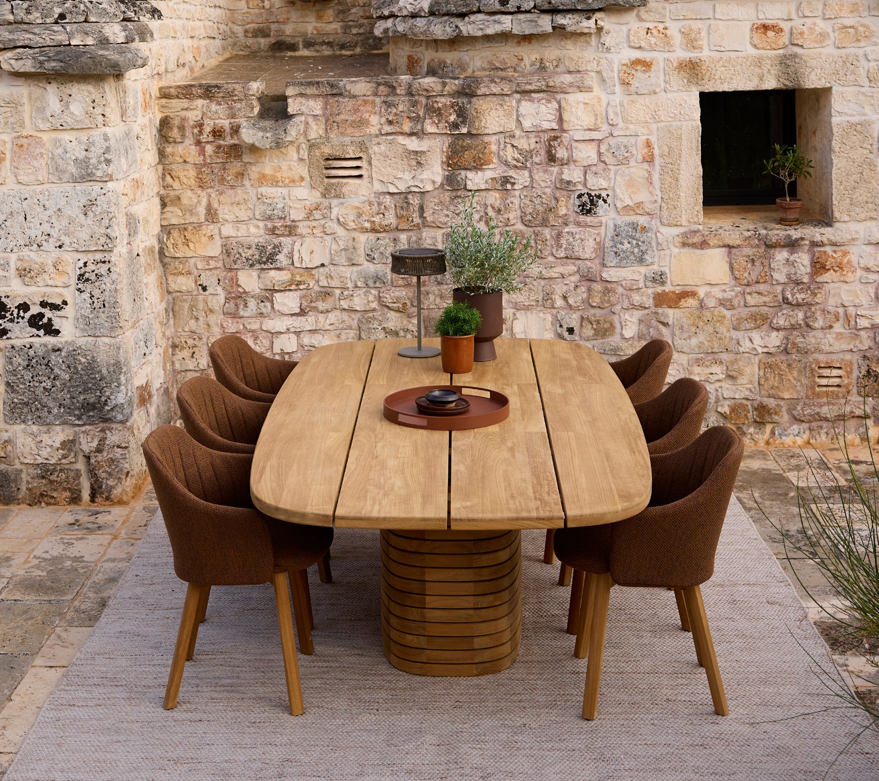 Modern houten eettafel omringd door bruine stoelen in een rustieke setting.