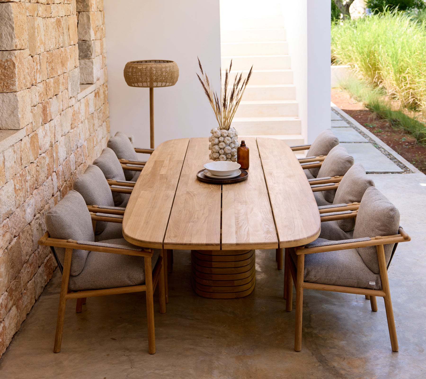 Moderne eetopstelling met houten tafel, grijze kussens en houten stoelen.