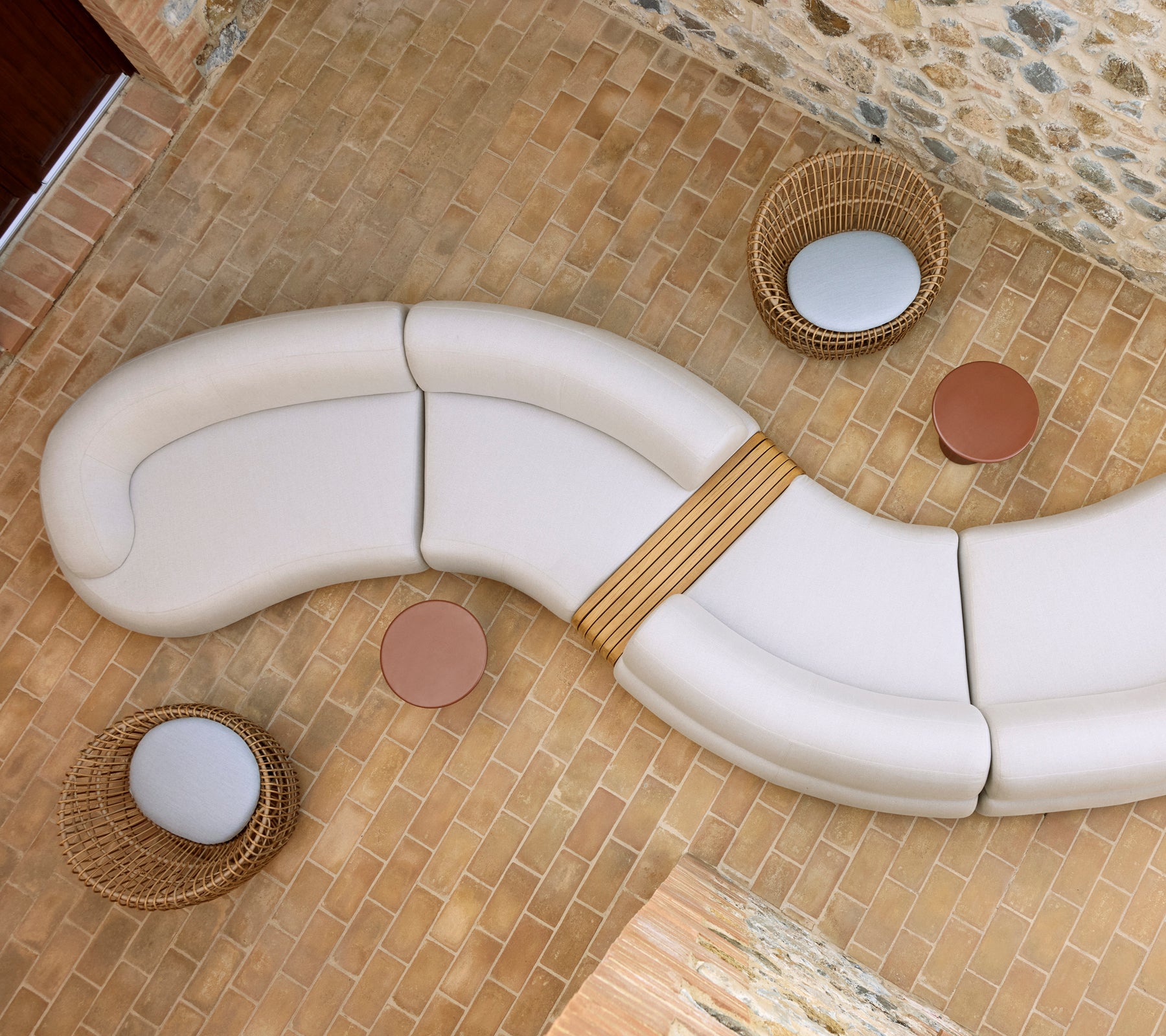 Ontspannen lounge met een gebogen witte zitopstelling, twee ronde Glaze salontafels en gevlochten Nest-stoelen op een stenen vloer.