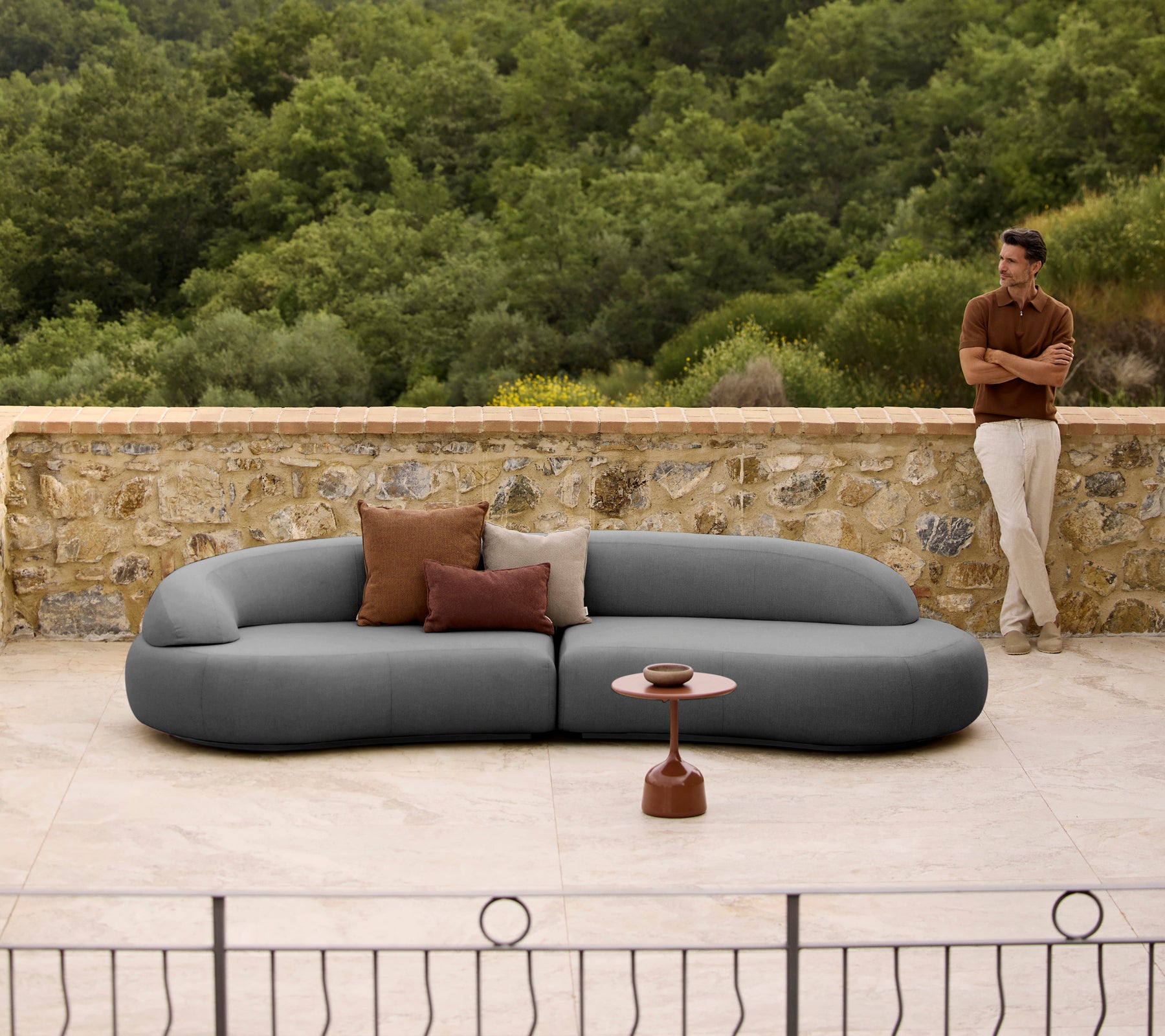 Mellow loungebank met kussens naast een strak Glaze salontafel, geplaatst tegen een natuurlijke achtergrond.