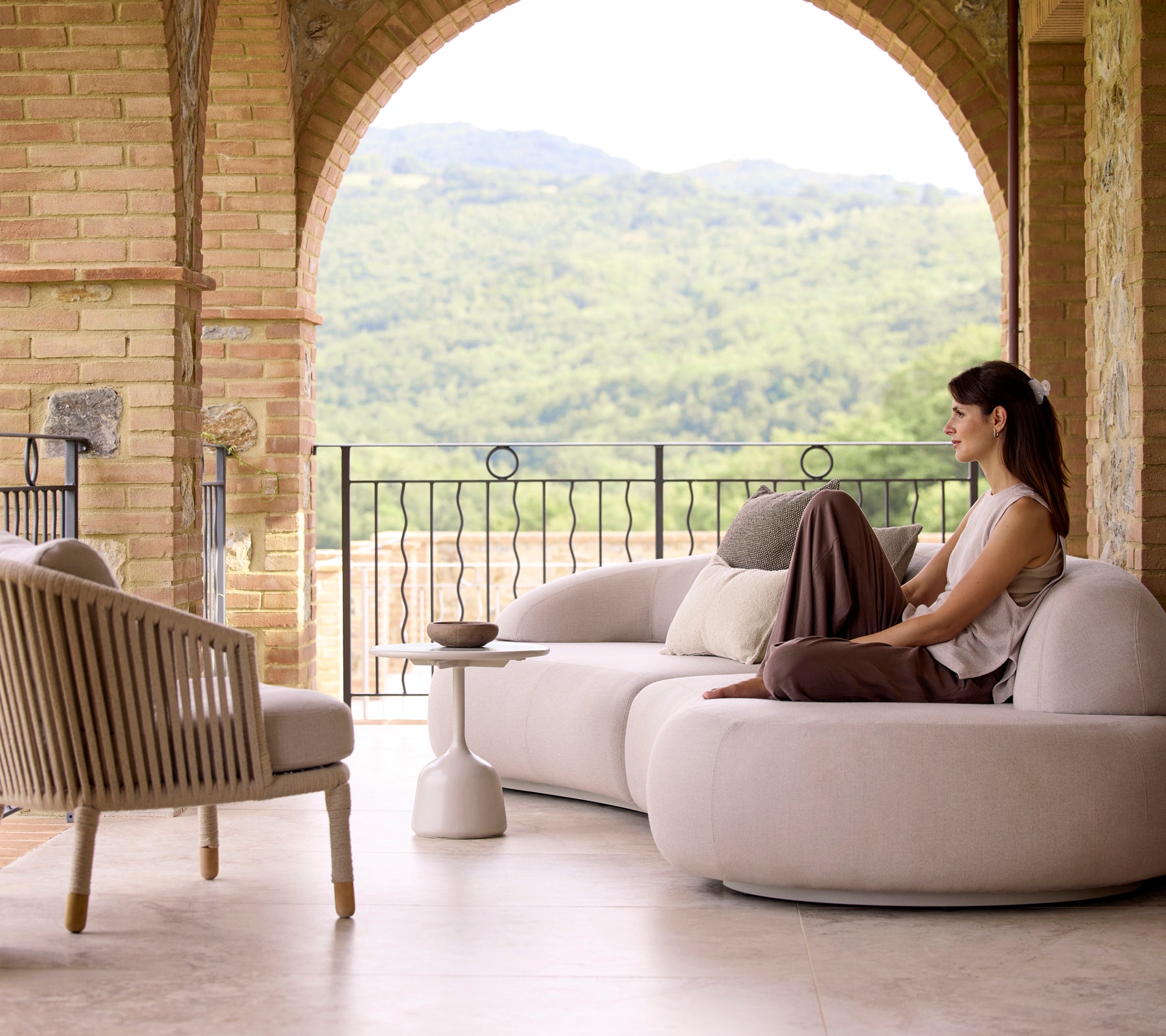 Een rustig zithoek met een zachte loungesofa, een Moments-loungechair en een Glaze salontafel, met weelderig groen op de achtergrond.