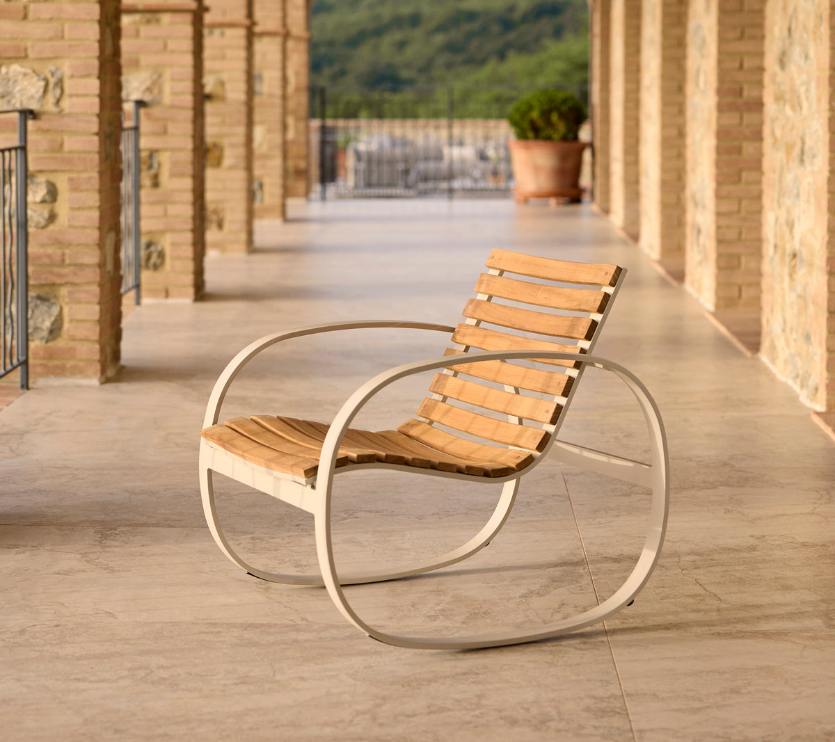 Parc schommelstoel met een aluminium frame en houten latten, gepositioneerd op een terras met stenen vloer en een schilderachtige achtergrond.
