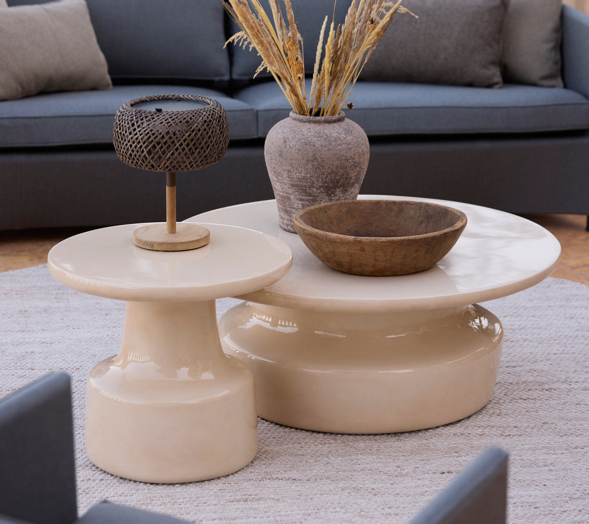 Moderne beige koffie- en bijzettafels met een bruine schaal en een metalen lamp in een lounge-instelling.