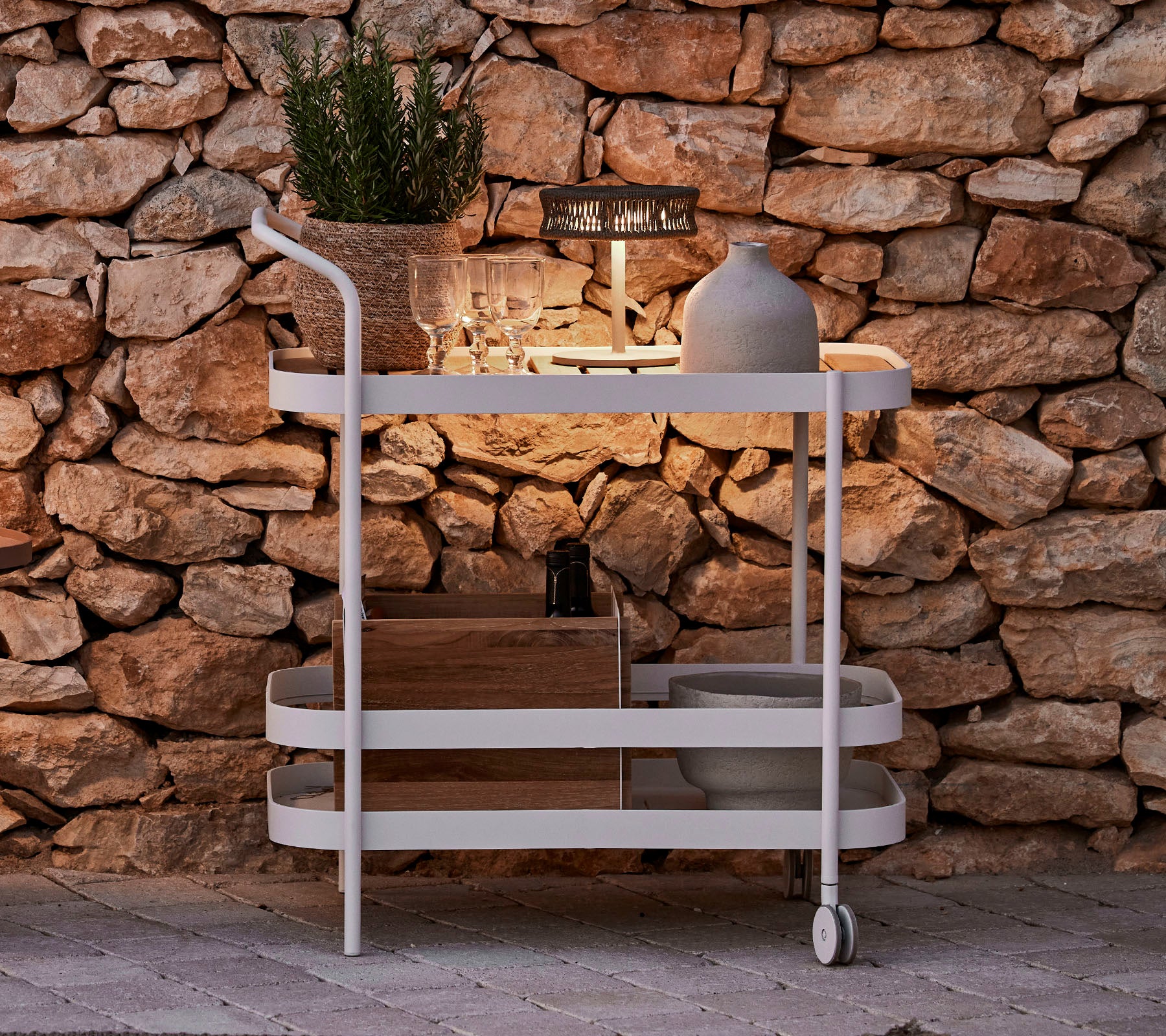 Een stijlvolle wagen met een houten bovenkant, witte frame, decoratieve pot en elegante verlichting tegen een stenen muur.