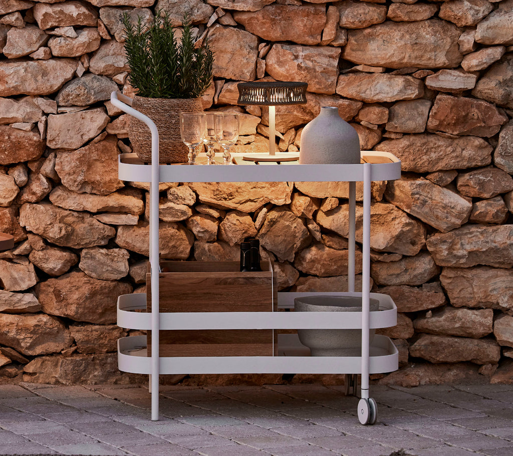Een stijlvolle wagen met een houten bovenkant, witte frame, decoratieve pot en elegante verlichting tegen een stenen muur.