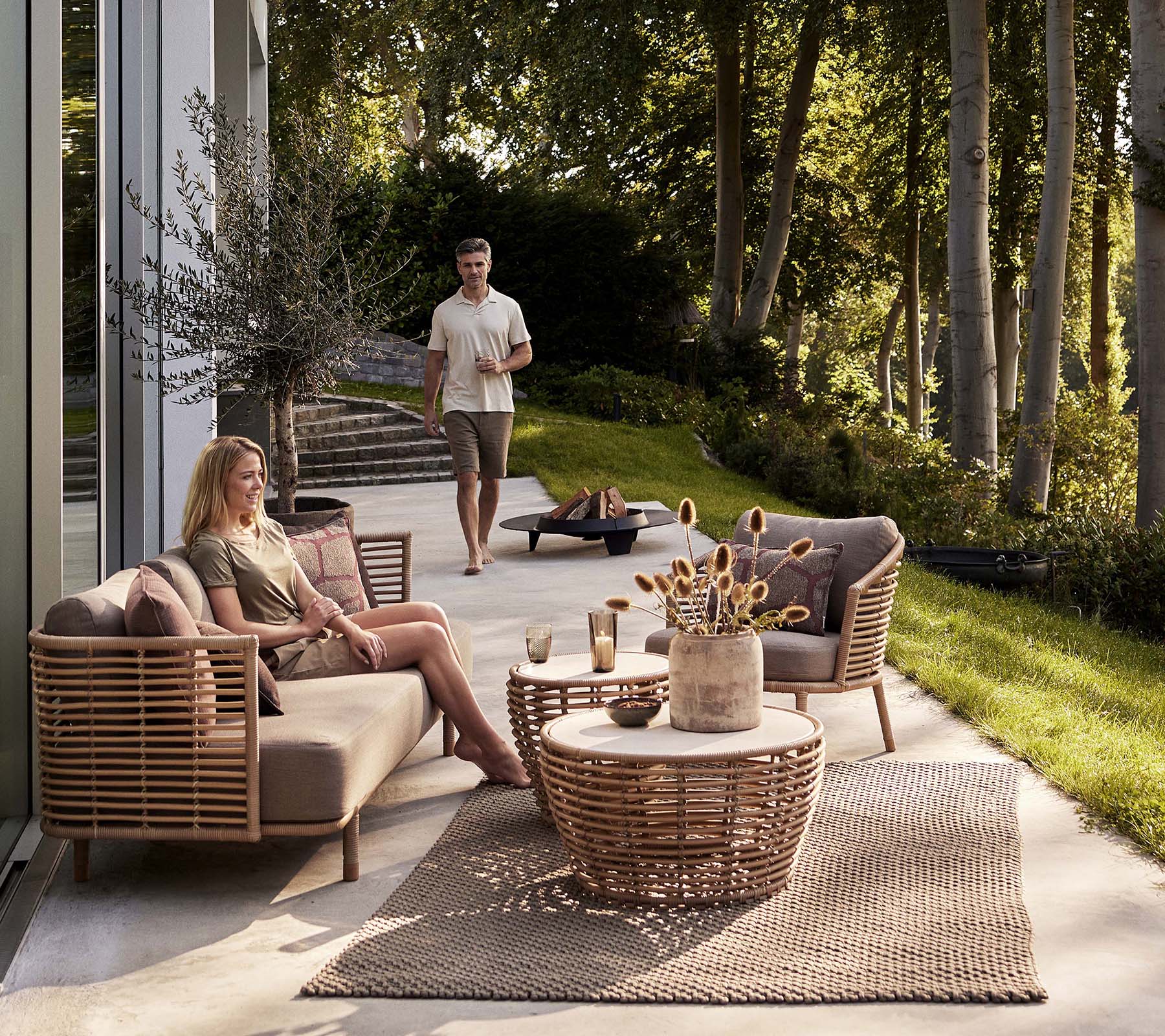Een gezellige zitruimte met een Sense-sofa en loungestoel, vergezeld van een mandkaffee-tafel en decoratieve elementen.