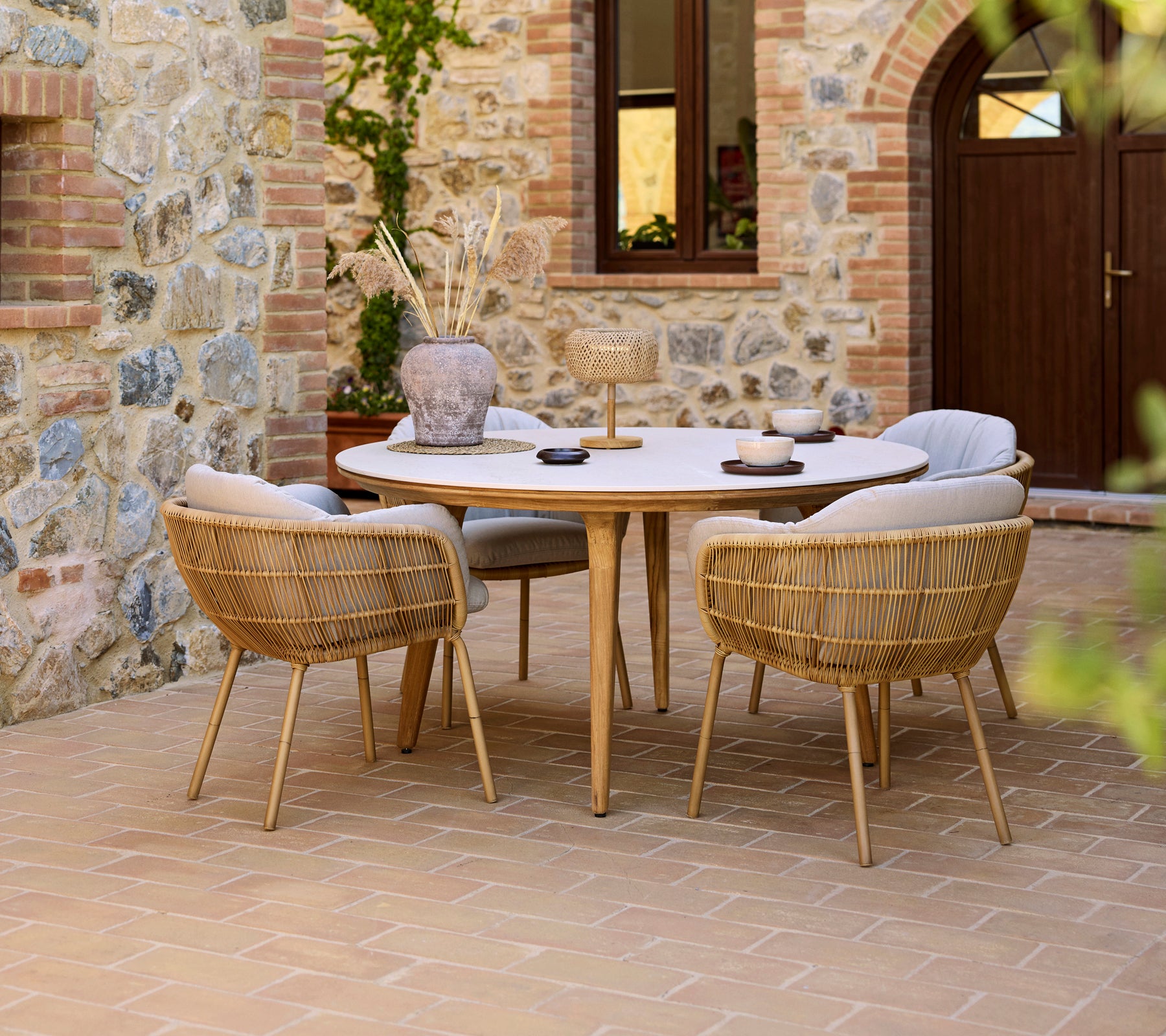 Buiten eetopstelling met een ronde Aspect tafel en Stay stoelen, tegen een stenen muur als achtergrond.