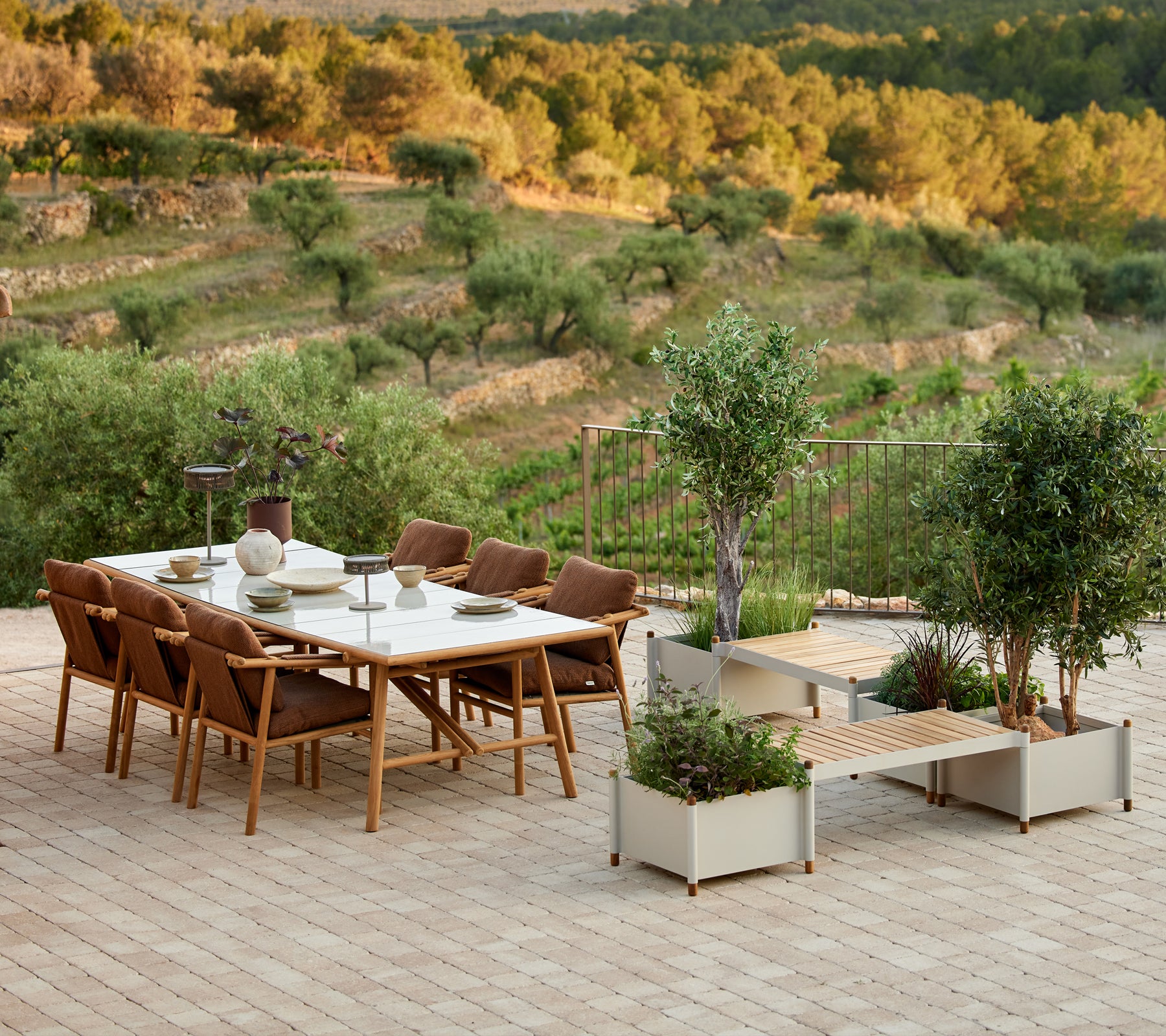 Stijlvolle teak eettafelset met stoelen en een plantenbank, omringd door groen en een pittoresk landschap.