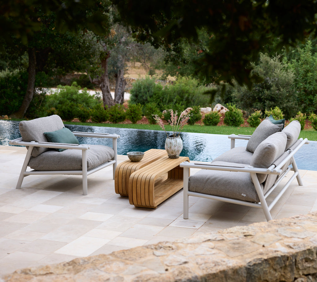 Modern loungegebied met witte stoelen met grijze kussens en een houten salontafel.