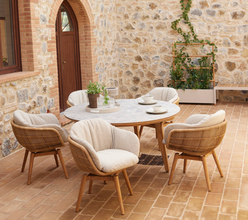 Een stijlvolle zithoek met ronde stoelen en een ronde tafel, aangevuld met groen in een plantenbak tegen een stenen muur.