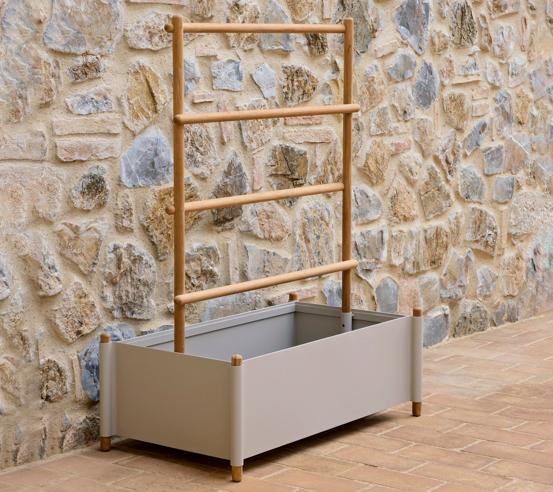 Een grijze aluminium plantenbak met een houten leuning, ontworpen voor het kweken van planten, tegen een gestructureerde stenen muur.