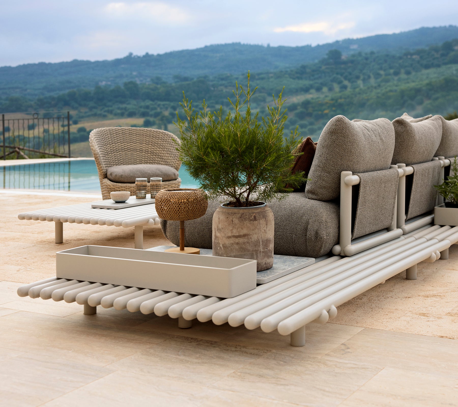 Een stijlvolle loungehoek met een comfortabele stoel, een opbergdoos en een elegante platform van aluminium, omringd door groen.