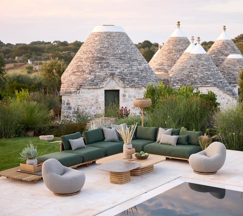 Moderne loungegebied buiten met een groene sectional bank, grijze fauteuils en een houten salontafel.