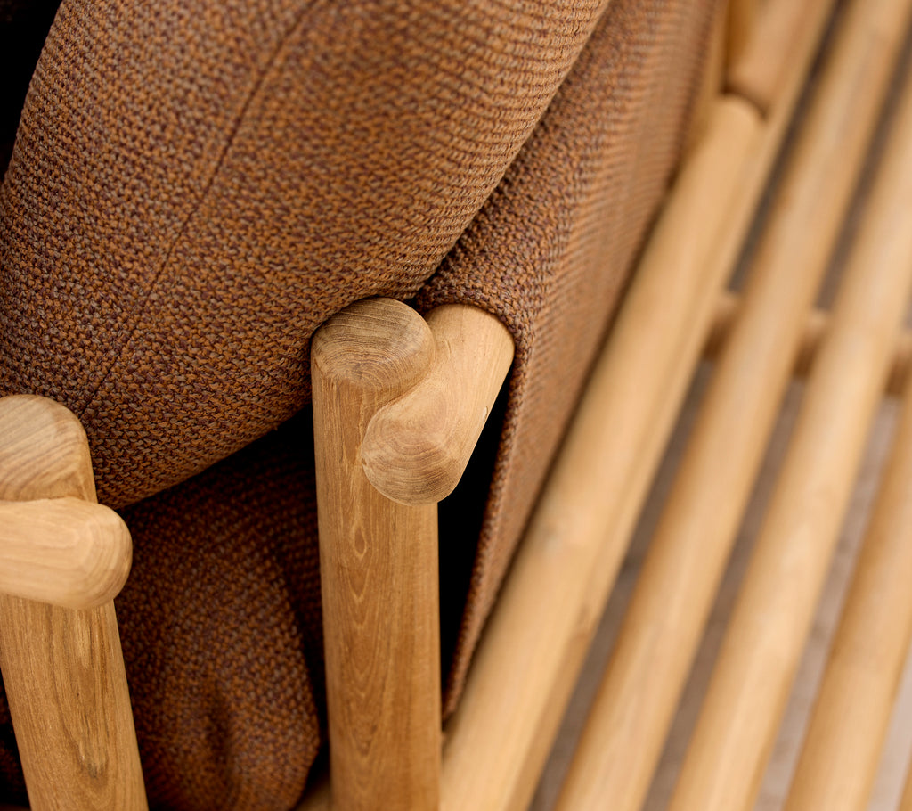 Teak loungestoel met zachte kussens en stijlvolle houten staven die de armleuning en basisstructuur vormen.