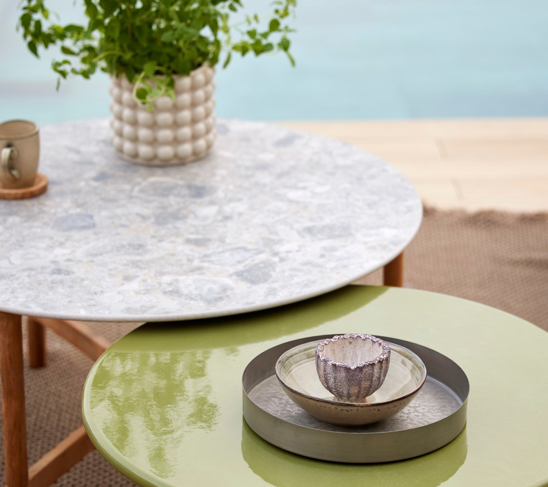 Een Twist tafel in meerdere kleuren met een geglazuurde lava stenen bovenkant, vergezeld van een decoratieve kom en plant in een stijlvolle setting.
