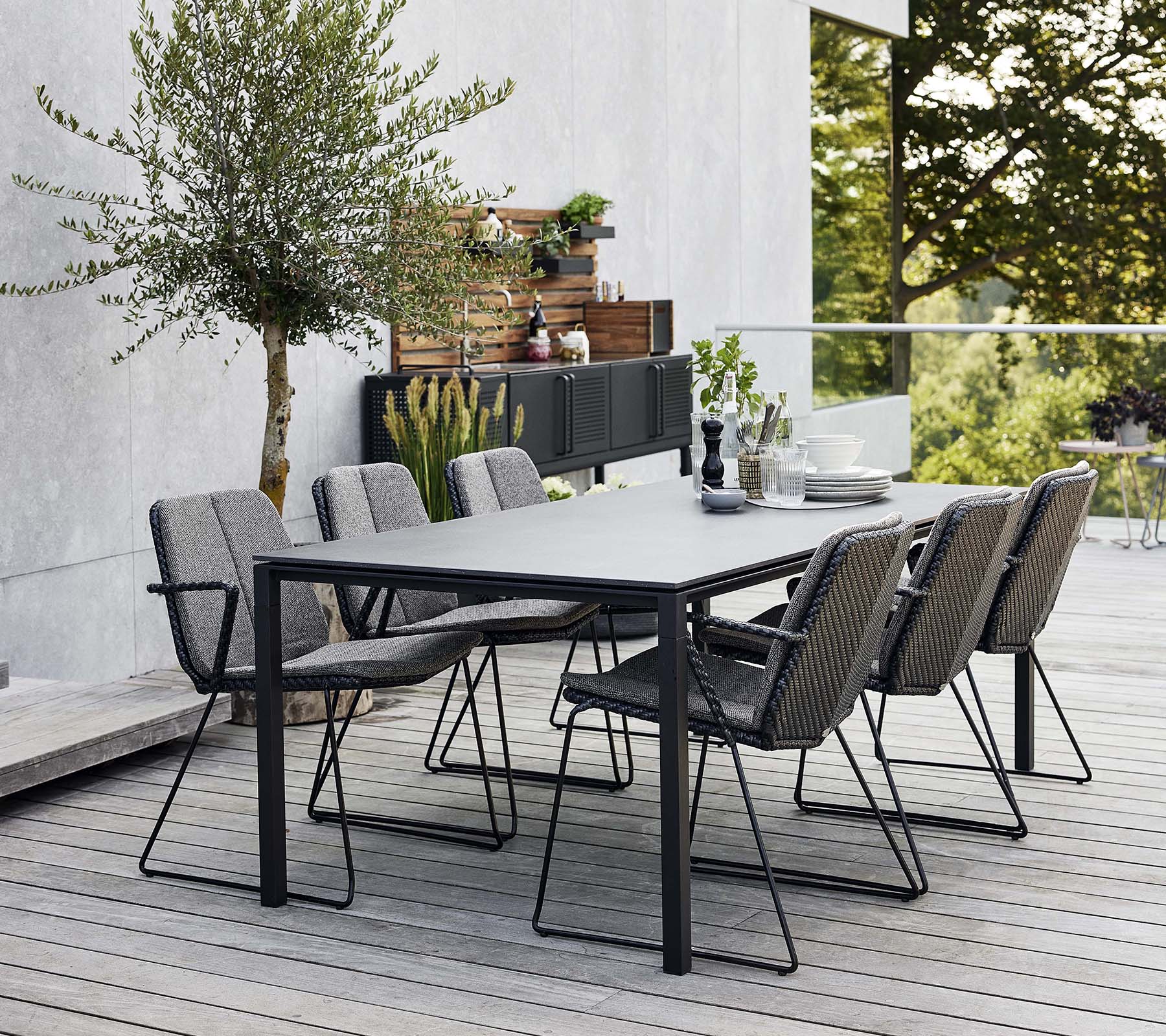 Een stijlvolle eetset voor buiten met een slank tafel en verschillende comfortabele armstoelen, omringd door groen en een moderne achtergrond.