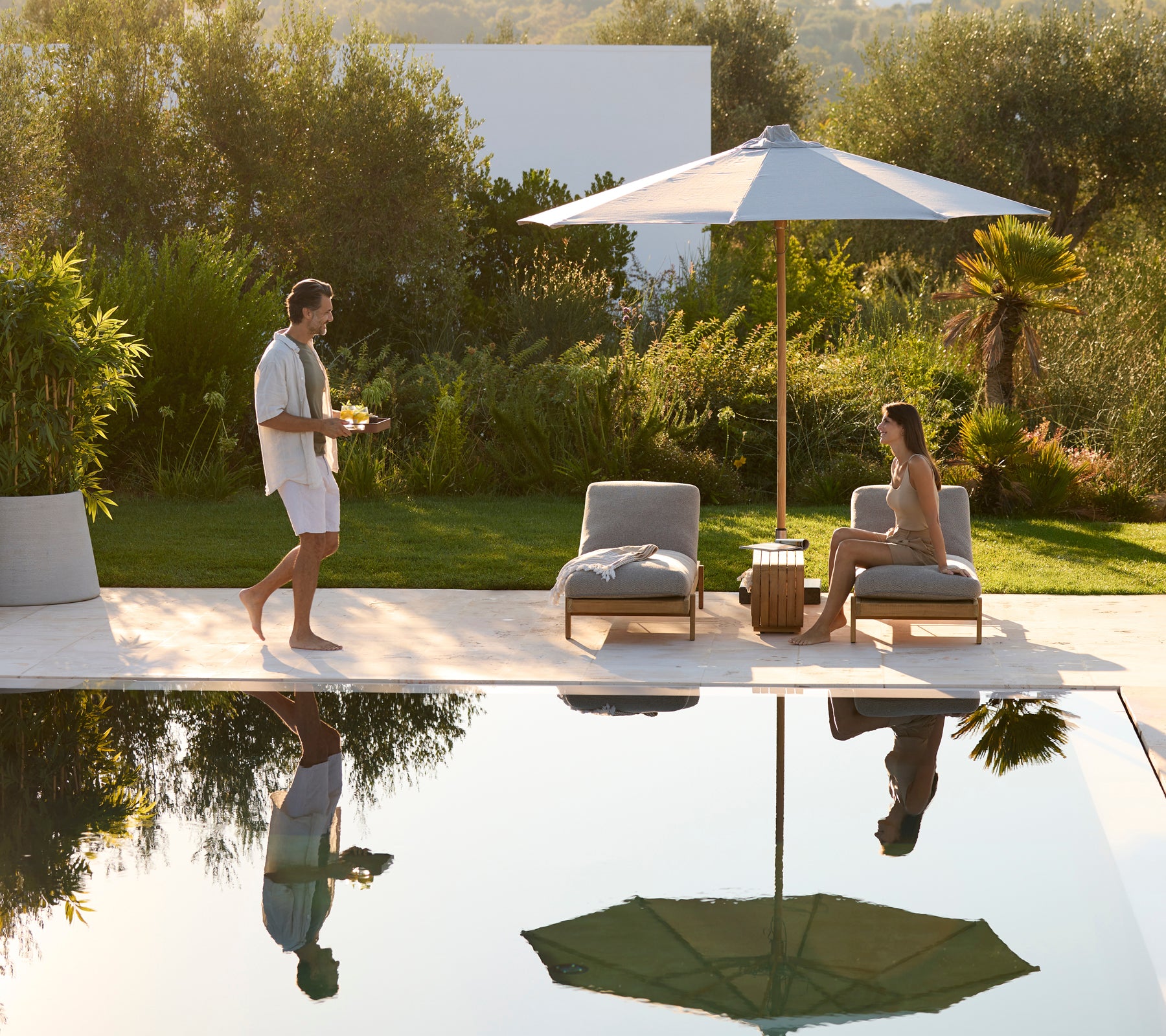 Moderne buitentuin met grijze stoelen, een houten tafel en een groene parasol.