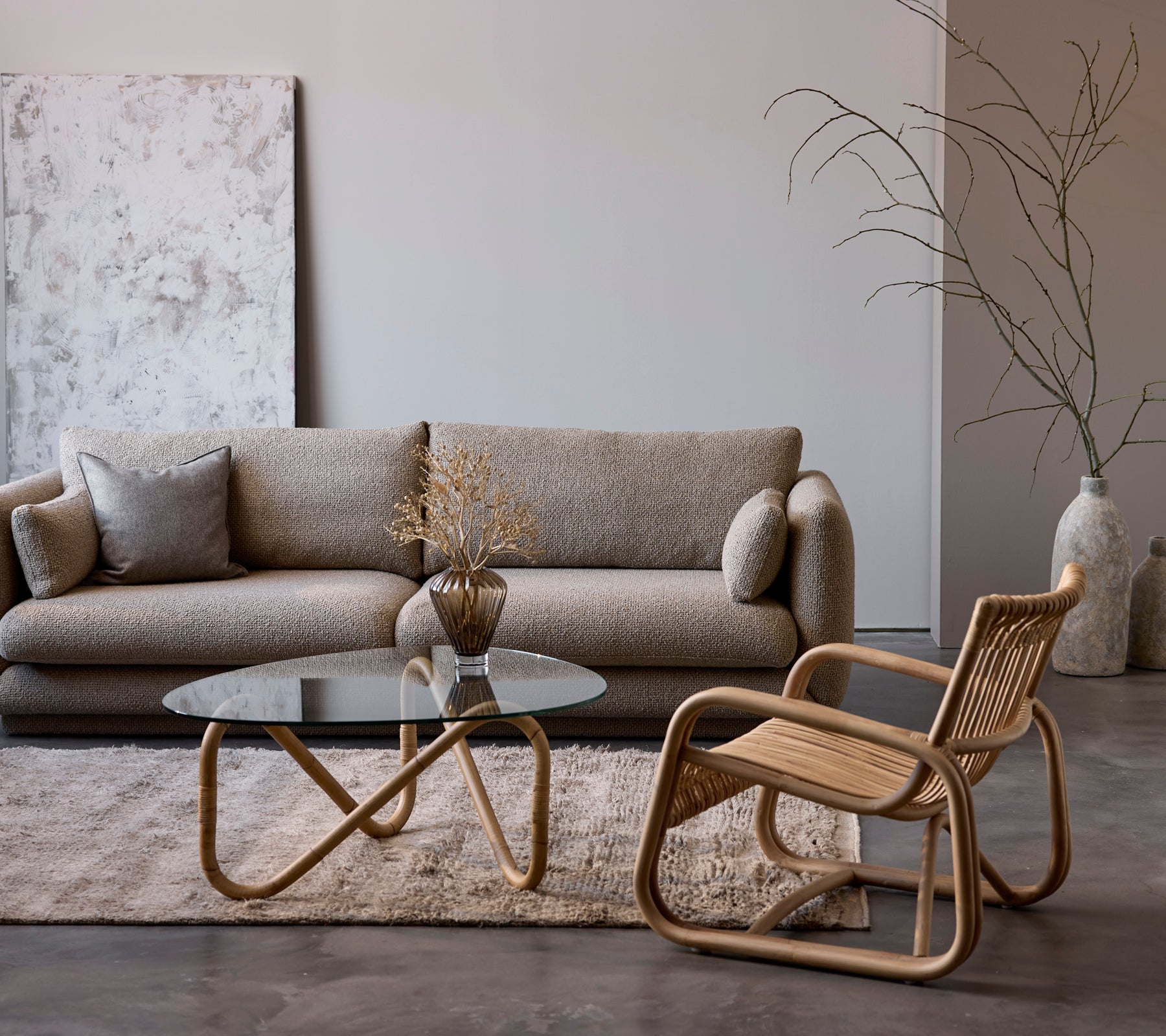 Moderne lounge-opstelling met een beige bank, glazen tafel en gehaakte stoel.