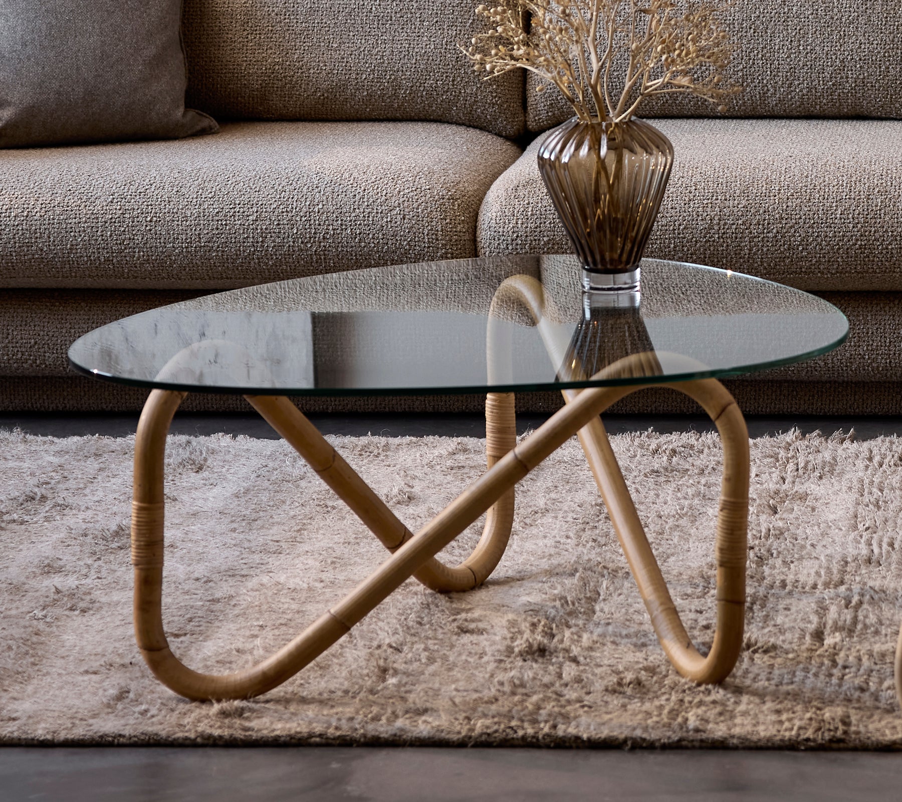 Modern glazen salontafel met een beige vaas op een tapijt in een lounge-setting.