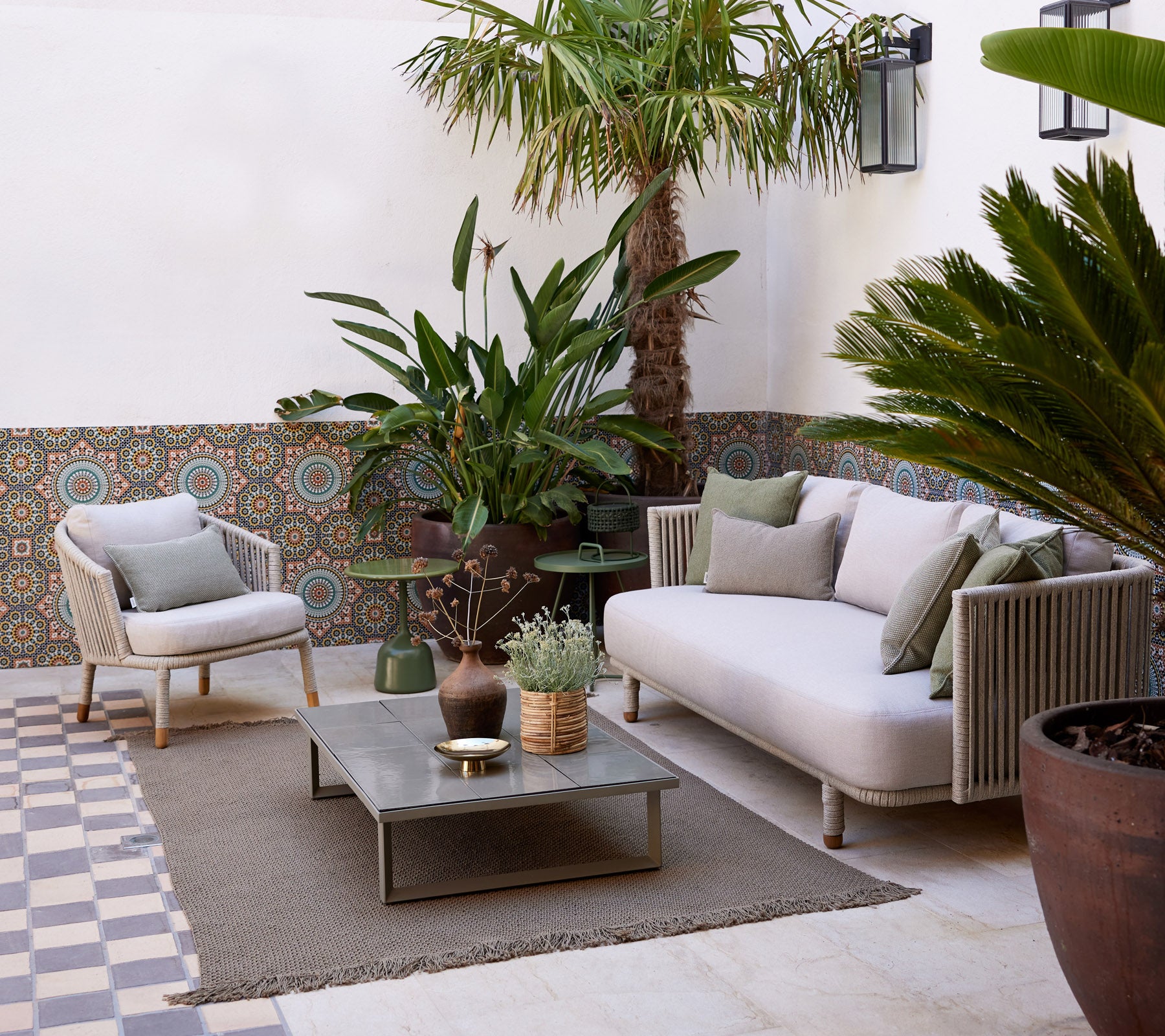 Gezellige loungeruimte met een lichte bank, potplanten, een decoratieve tafel en een gestructureerde vloer die een serene sfeer creëert.