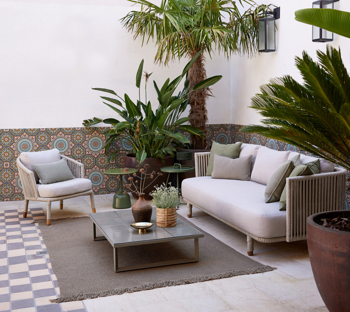 Gezellige loungeruimte met een lichte bank, potplanten, een decoratieve tafel en een gestructureerde vloer die een serene sfeer creëert.