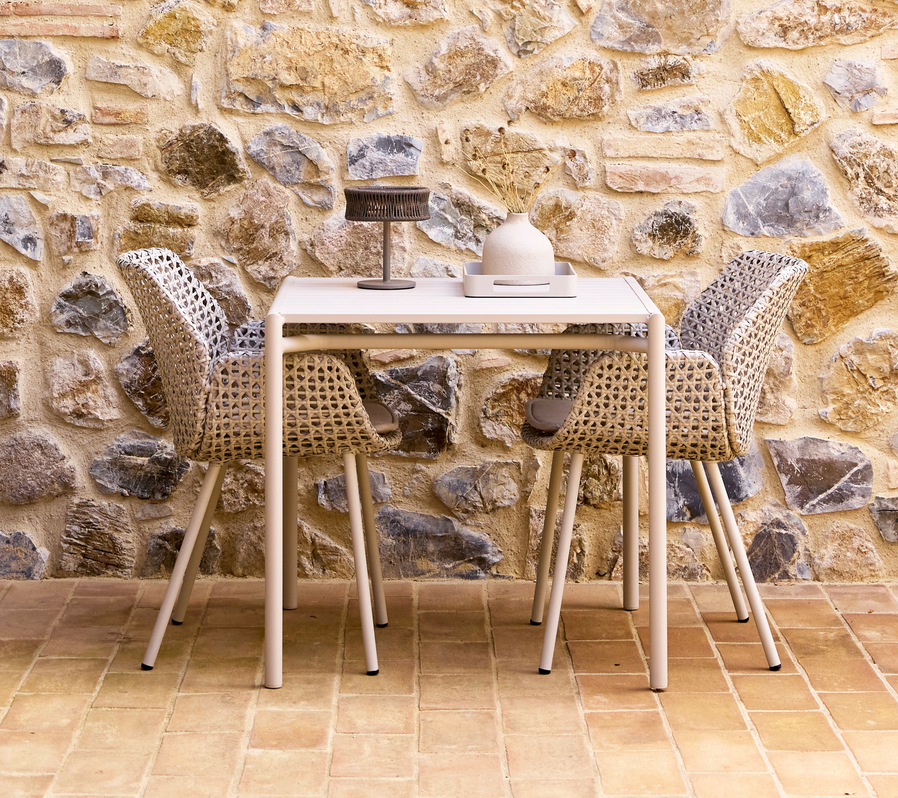 Een stylish eetset met zandkleurige stoelen rond een moderne tafel, tegen een gestructureerde stenen muur.